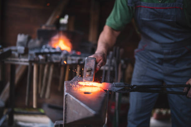Craftsman forges molten metal on an anvil. An unrecognizable blacksmith forges hot metal with a hammer on an anvile. blacksmith shop photos stock pictures, royalty-free photos & images