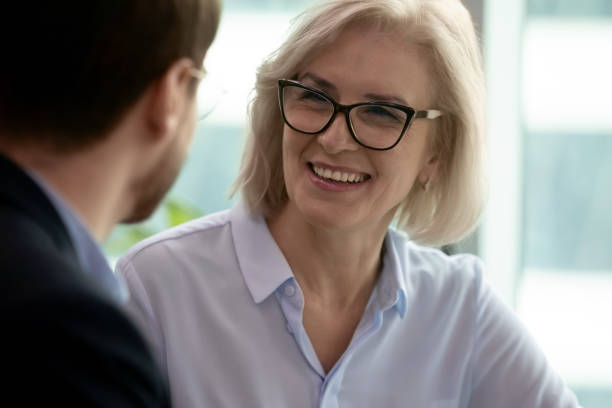 onder-oude onderneemster die met partner tijdens vergadering in bureau spreekt - gesprek coaching detail stockfoto's en -beelden
