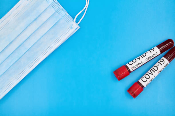conceptual photo. face mask and blood test samples for presence of coronavirus. tubes containing blood samples that have tested positive and negative for coronavirus. blue background, copy space - blood sample imagens e fotografias de stock