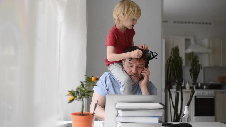 Man working from home with laptop during quarantine. Home office and parenthood at the same time. Exhausted parent with hyperactive child.