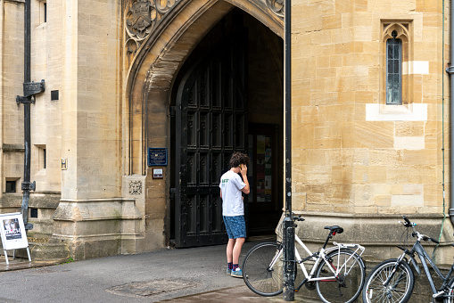 A young man using his phone outside the Bodleian Library and All Souls College at the university of Oxford. Oxford, Oxfordshire, England, UK