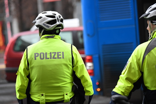 Unrecognizable back turned German policemen with helmets and yellow reflective jacket riding bikes