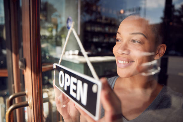 female owner of start up coffee shop or restaurant turning round open sign on door - business owner imagens e fotografias de stock