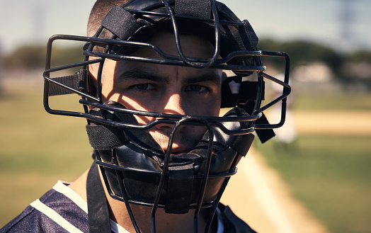 Portrait of a young man wearing a catchers helmet while playing a game of baseball