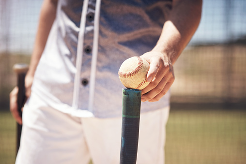 Cropped shot of a man holding a ball on top of his batting tee at a baseball game