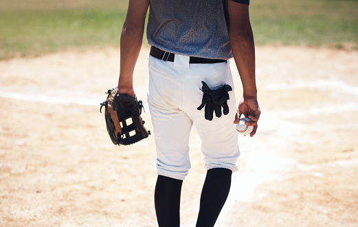 Cropped shot of a man standing on a field and holding a baseball mitt and ball at a match