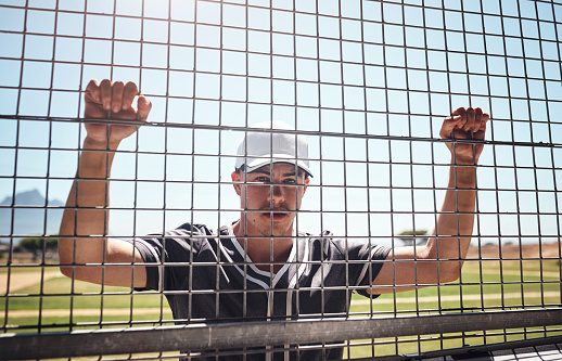 Shot of a young man watching a game of baseball from behind the fence