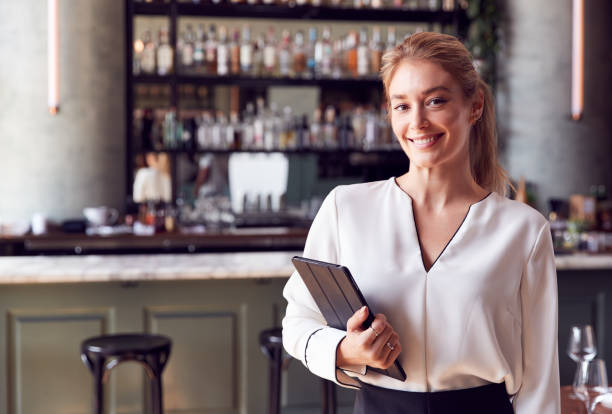 Portrait Of Confident Female Owner Of Restaurant Bar Standing By Counter Holding Digital Tablet Portrait Of Confident Female Owner Of Restaurant Bar Standing By Counter Holding Digital Tablet franchising photos stock pictures, royalty-free photos & images