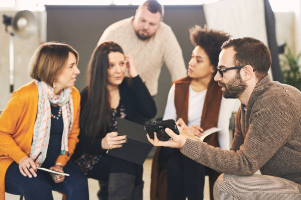istock Young handsome bearded educator showing to his multicultural attendees how camera works. Photo studio interior. 1226420599