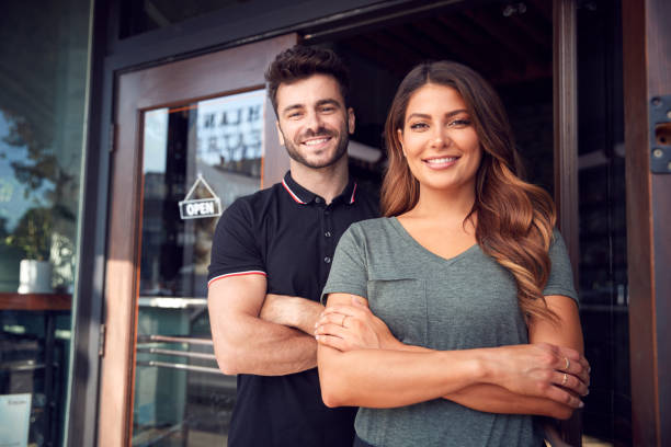 Portrait Of Couple Starting New Coffee Shop Or Restaurant Business Standing In Doorway Portrait Of Couple Starting New Coffee Shop Or Restaurant Business Standing In Doorway franchising photos stock pictures, royalty-free photos & images