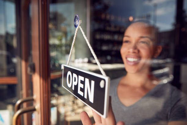 la proprietaria femminile di una caffetteria o di un ristorante di start up che gira segno aperto sulla porta - owner small business restaurant african ethnicity foto e immagini stock