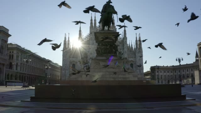 Flock of pigeons flying in front of the Duomo di Milano (Milan Cathedral) in Piazza del Duomo (Duomo square) in front of the statue of Vittorio Emanuele II during the pandemic lockdown in 2020. Empty city in the morning.