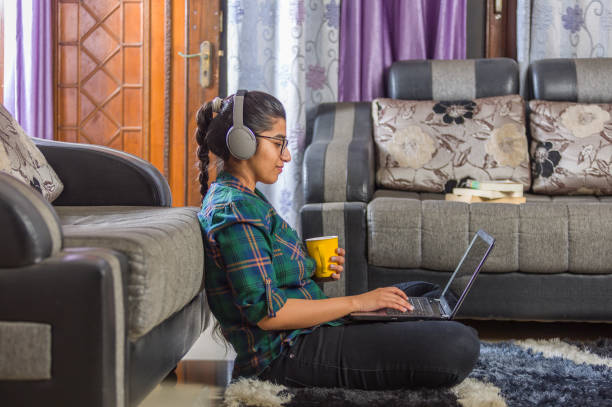 une fille indienne utilisant l’ordinateur portatif, s’asseyant sur l’étage - indian ethnicity audio photos et images de collection