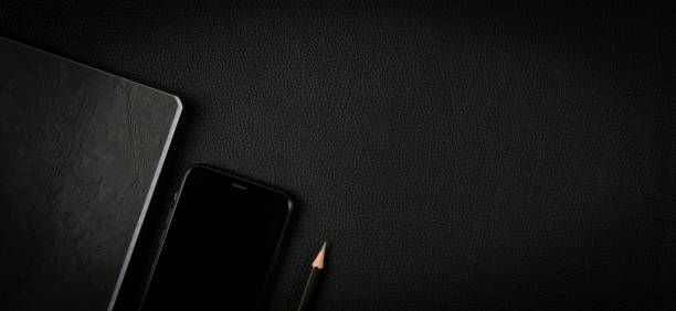 black color notebook, mobile phone, Pencil on natural real black leather surface background, studio top close up view photography, copy space on right.