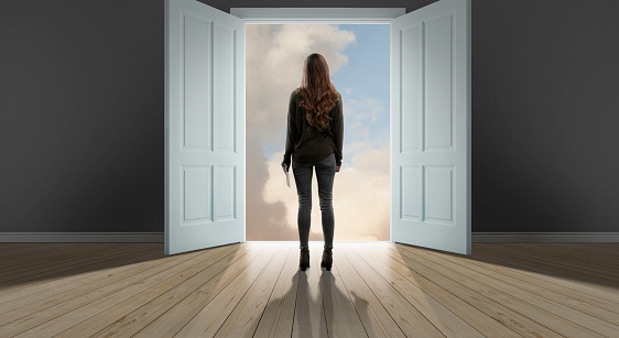 A woman standing in front of large doors with sky behind them