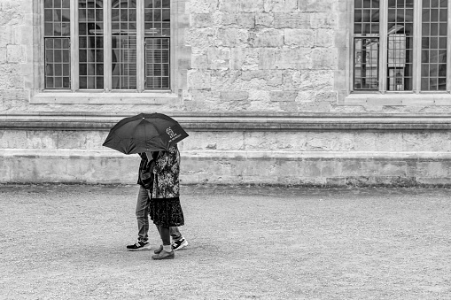 Two young women under an umbrella outside the Bodleian Library and All Souls College at the university of Oxford. Oxford, Oxfordshire, England, UK