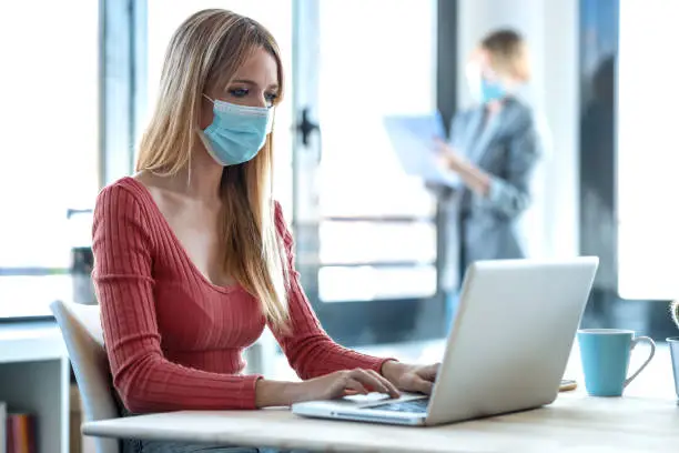 Shot of business young women wearing a hygienic facial mask working in the office while keeping safe distances.