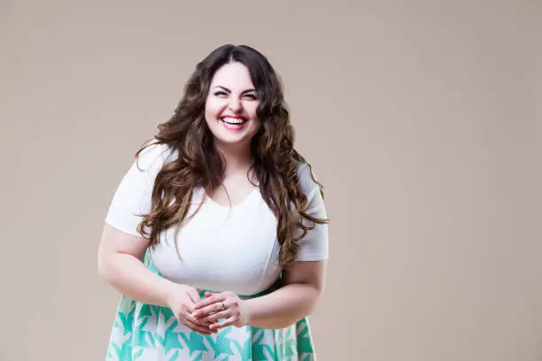 Laughing happy plus size model in casual clothes, fat woman on beige background, body positive concept