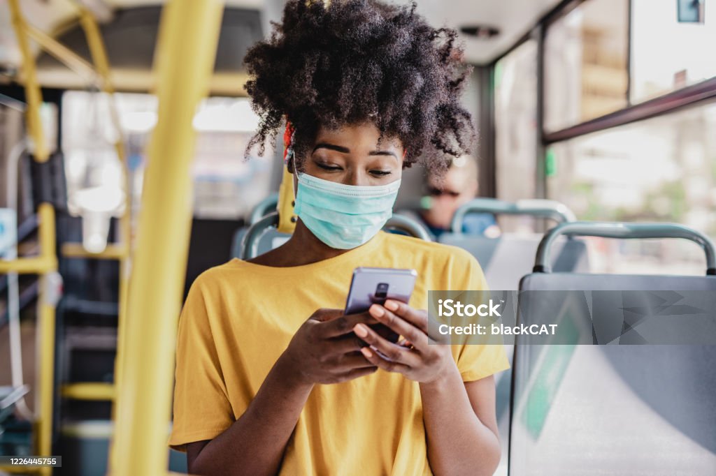 Commuting during a pandemic African American woman wearing a protective mask while sitting in a bus and using a mobile phone Bus Stock Photo