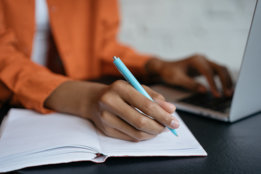 Toma de primer plano de la mano del estudiante sosteniendo la pluma y escribiendo en el cuaderno, trabajando en casa. E-learning photo