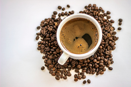 Top view of black coffee in white cup, with roasted fresh beans around. Coffee cup and coffee beans on white background. Black coffee in a coffee cup top view isolated on white background.