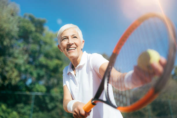 senior tennis – pretty mature woman serving ball in tennis - tennis serving playing women imagens e fotografias de stock