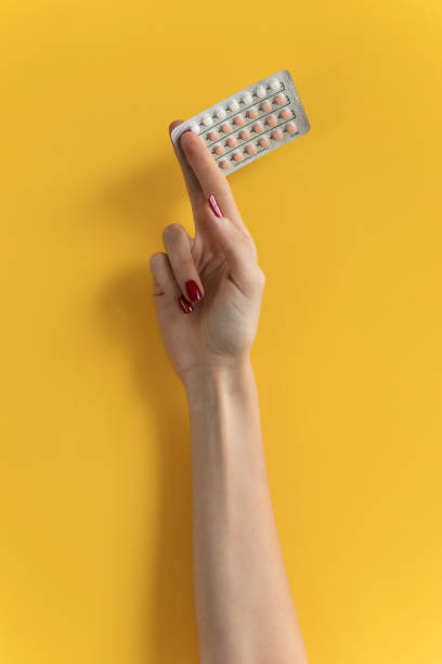 female hand holding contraceptives against a yellow background. - contraceção imagens e fotografias de stock