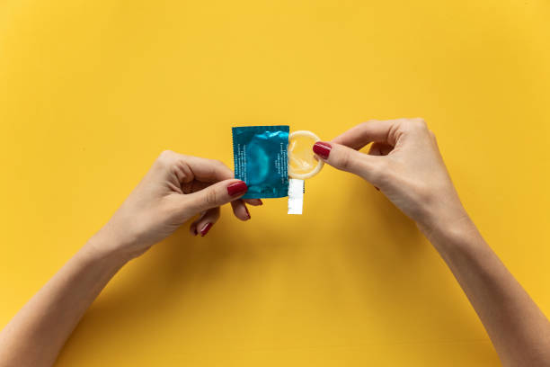 jovem segurando preservativo pronto para usar para sexo seguro sobre fundo amarelo. - sexual issues aids condom human pregnancy - fotografias e filmes do acervo