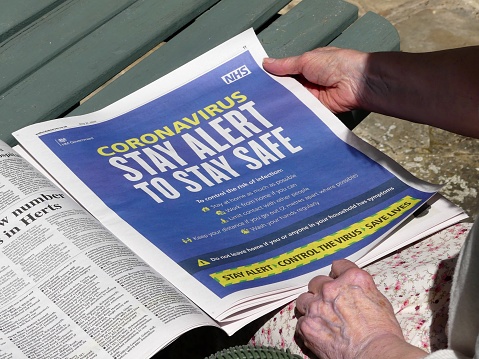 Chorleywood, Hertfordshire, England, UK - May 22nd 2020: Elderly woman reading Coronavirus Stay Alert to Stay Safe advertisement, issued by HM Government and NHS, in local newspaper