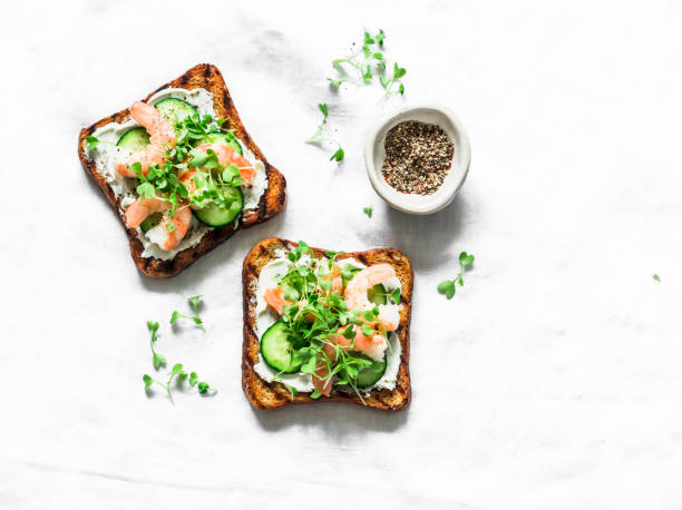 istock Grilled whole grain bread cream cheese shrimp cucumber micro greens sandwiches on a light background, top view 1226467646