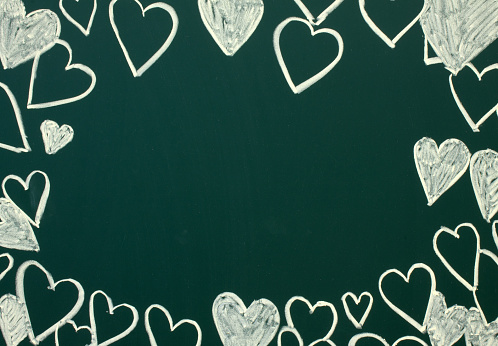 A frame of chalked hearts on a green blackboard close up and space for copying