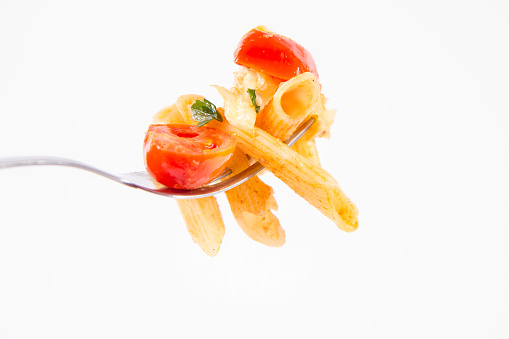 Penne with tomatoes, garlic and mozzarella on a fork held by a woman's hand on a white background