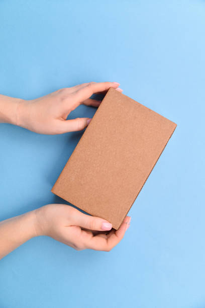 istock Female hands holding present box or gift box package in craft paper over blue background. Top view, flat lay 1226470645