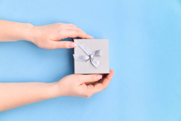 istock Female hands holding present box or gift box package in craft paper over blue background. Top view, flat lay 1226470730