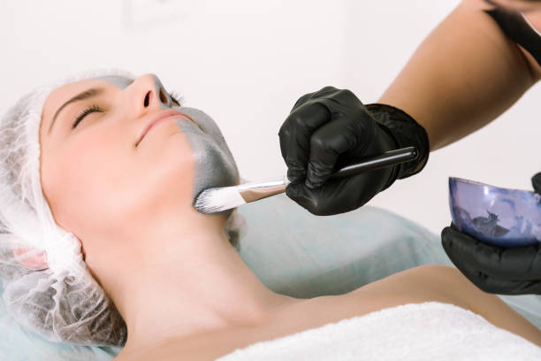 Cosmetologist's hand in a protective rubber glove uses a special brush to apply a silver ointment to a female patient's neck lying on a pillow