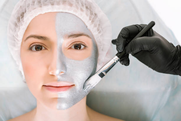 istock Nice woman looks directly into the camera while lying on a cosmetology table and applying a silver beauty mask to her skin with a brush. Skin cleansing and rejuvenation concept 1226479105
