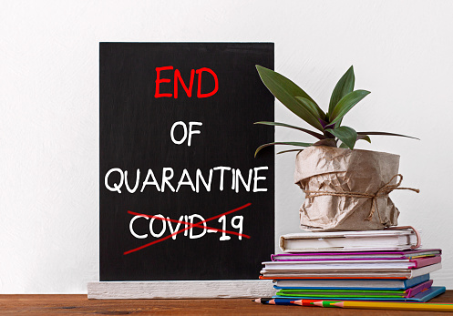 End of Quarantine COVID-19 sign on chalboard. Books stack, pencils with green home plant on white background. Distance education, e-learning, online learning lessons banner, open school classes.