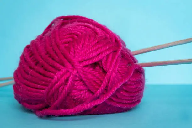Woolen yarn pink and knitting needles against blue background. Close up view. Selective focus.