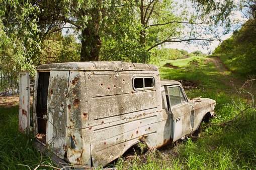 Old wrecked car with holes from beige bullets in an abandoned forest field