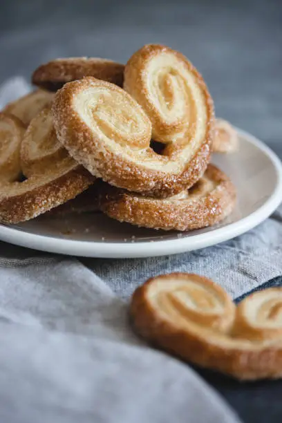 Photo of Palmier Puff Pastry. Delicious french palmier cookies with sugar on a white plate on dark background.