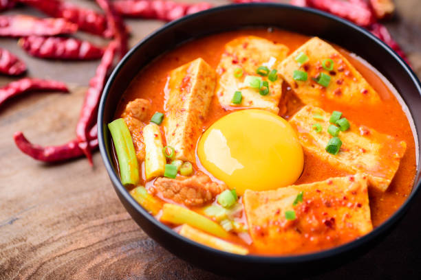 Asian woman holding a piece of kimchi and tteokbokki while enjoying Korean kimchi soup