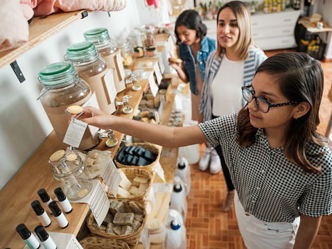A hispanic everyday woman and two girls looking at eco-friendly products in a sustainable shop.