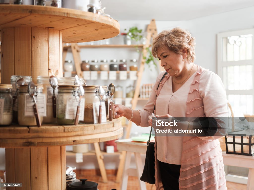 Hispanic senior woman shopping in zero waste store A hispanic senior woman standing and shopping for spices in zero waste store. Natural Beauty - People Stock Photo