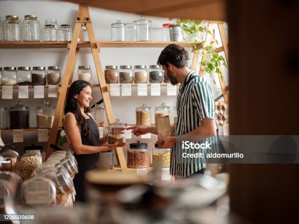 Happy Hispanic Employee Helping Young Man In Zero Waste Store Stock Photo - Download Image Now