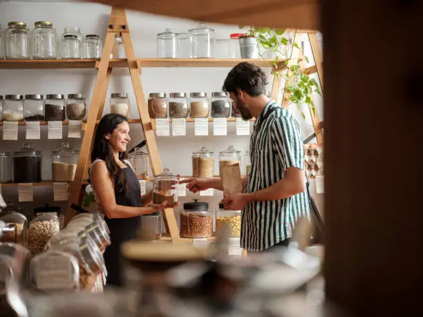 Photo of Happy hispanic employee helping young man in zero waste store