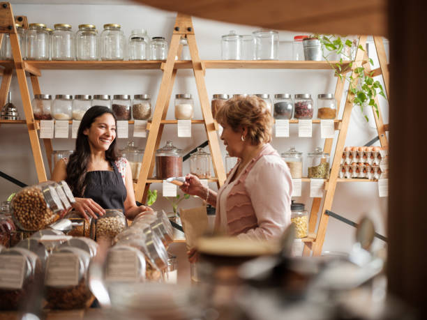 Happy hispanic employee and customer smiling at each other Happy hispanic employee and senior female customer standing next to the shelves of a sustainable shop and smiling at each other. plastic free photos stock pictures, royalty-free photos & images
