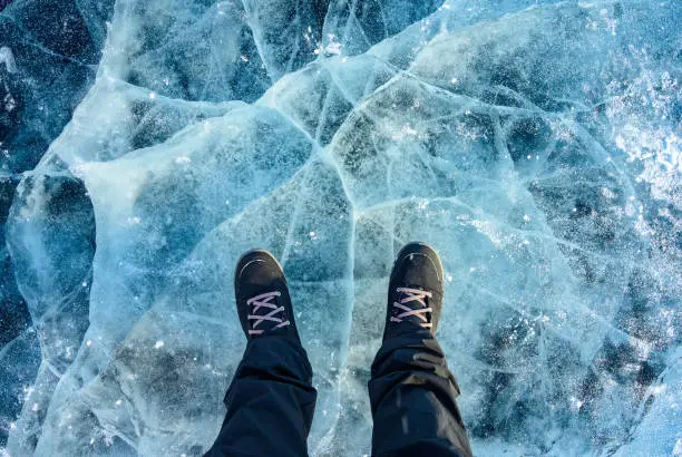 Photo of A foot of tourist standing on the cracks surface of frozen lake Baikal in the winter season of Siberia, Russia.