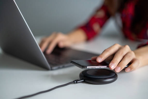 istock Young woman charge her phone with wireless charger while working with laptop 1226521630
