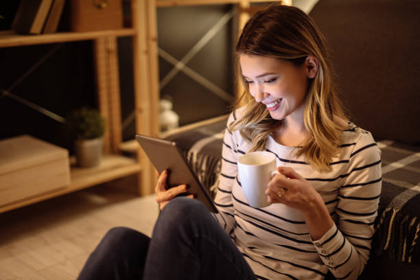istock Young woman using digital tablet and drinking tea at night in her living room 1226532176