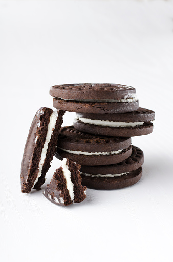 Stack of dark sandwich cookies and piece of it on the white background